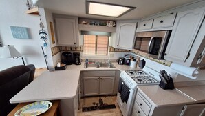 Una cocina compacta con gabinetes blancos, una estufa a gas, un microondas y un lavamanos. Hay una cafetera, un tostador y un escurreplatos.