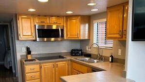 A compact kitchen with wooden cabinets, a stainless steel microwave, a toaster, and a sink. There are two stools at the island. - Oceanview Cabin 21 Jacuzzi Large Deck w View (Smith River)