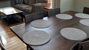A dining area with a dark wooden table, four round placemats, a sofa, and a window with blinds. - Oceanview Cabin 21 Jacuzzi Large Deck w View (Smith River)