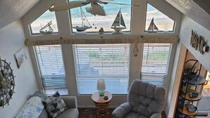 Un salon chaleureux avec un plafond haut, un ventilateur de plafond et une vue sur la plage grâce à de grandes fenêtres.