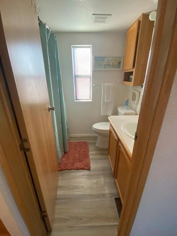 Un couloir étroit mène à une salle de bain équipée de toilettes, d’un lavabo et d’un espace douche.