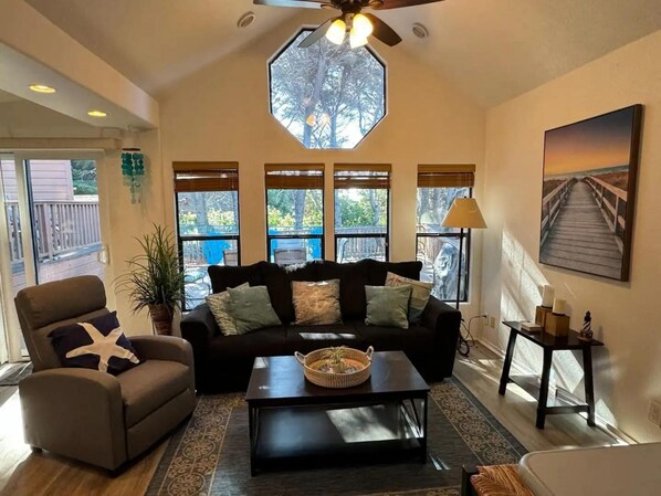 A spacious living room with a large window, a ceiling fan, and a painting on the wall.