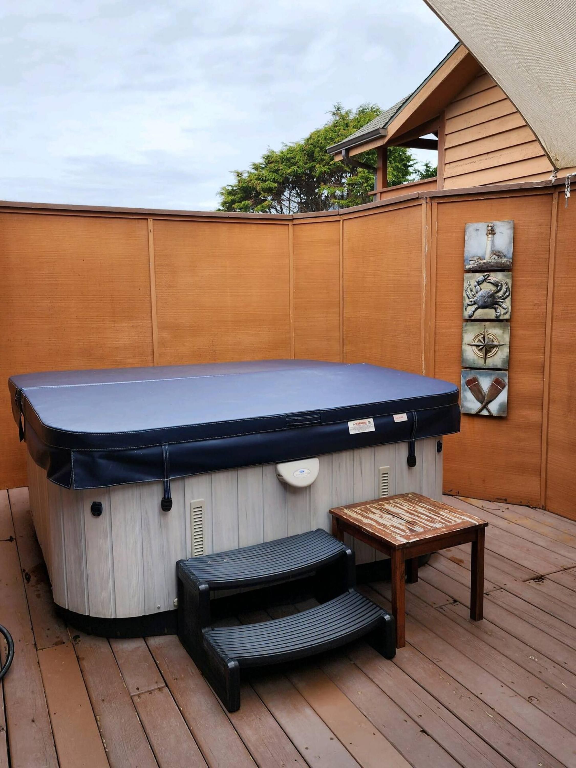 A hot tub with a cover, a wooden deck, a small table, and a bench.