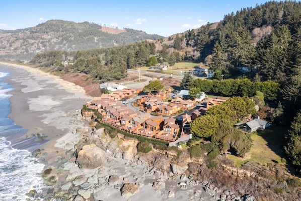 A coastal resort with terraced buildings, a beach, and forested hills in the background.