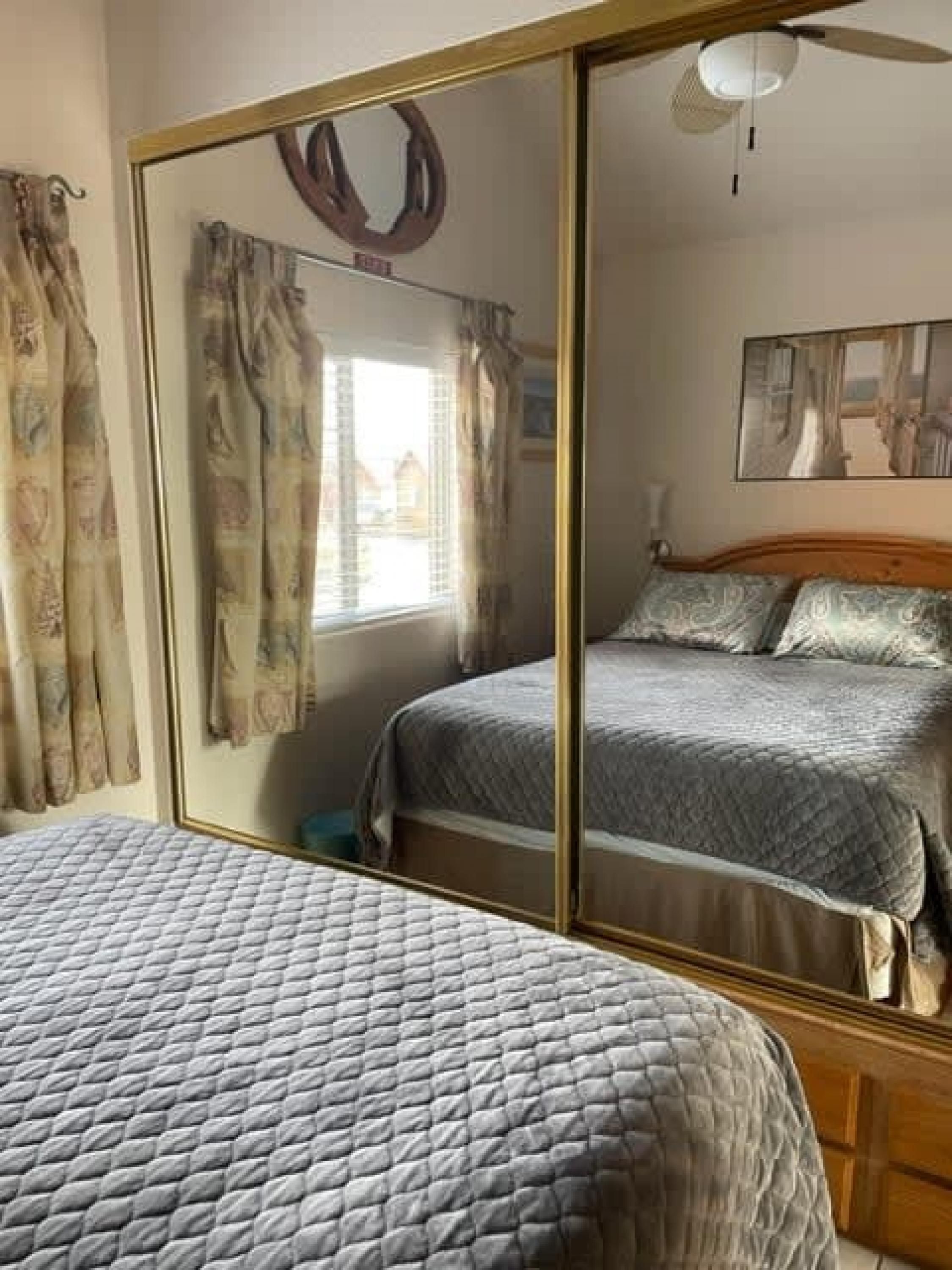 A bedroom with a mirrored wardrobe, a bed with a quilted cover, and a window with curtains.