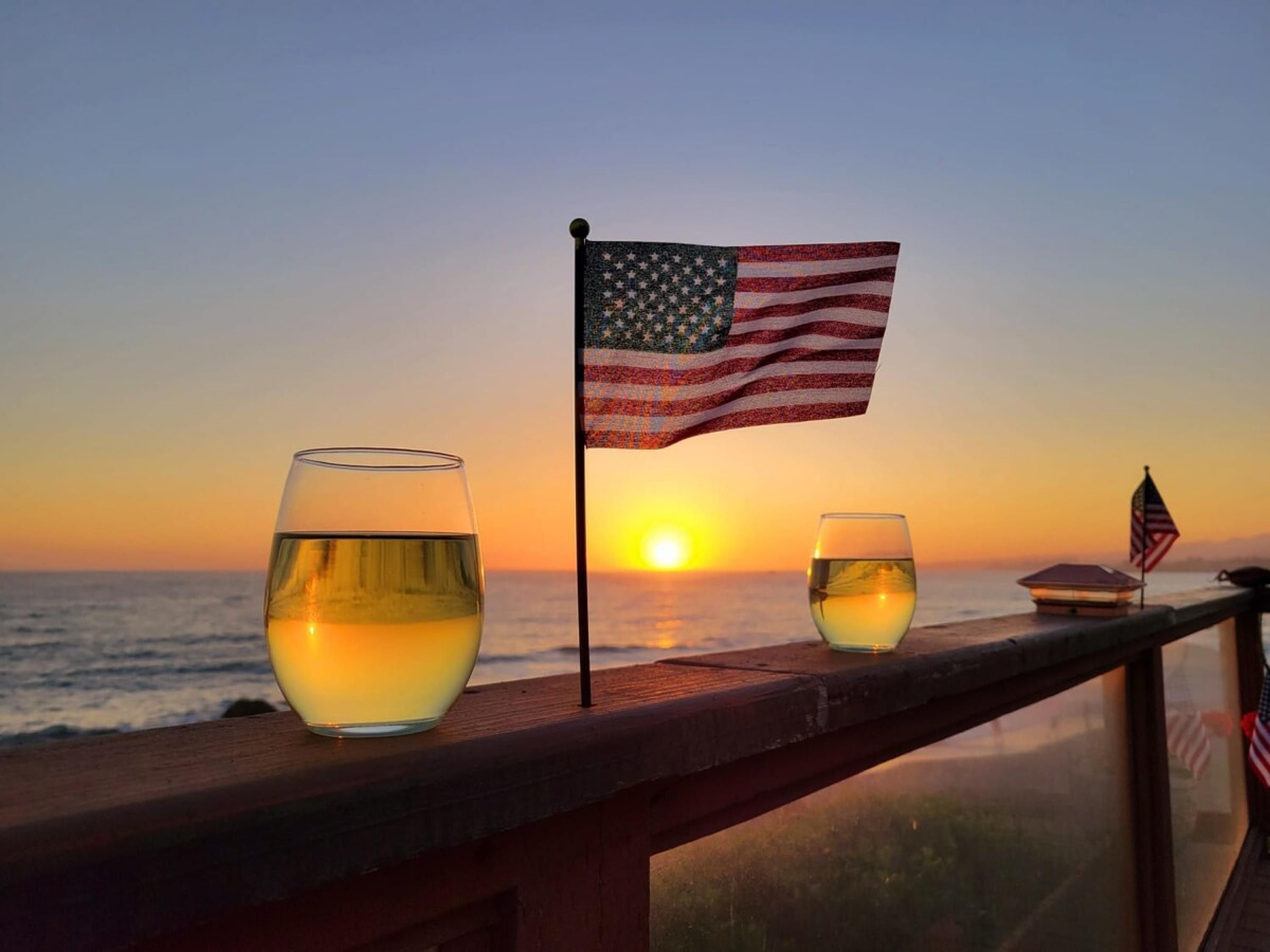 A sunset view from a balcony with two glasses of wine and an American flag.