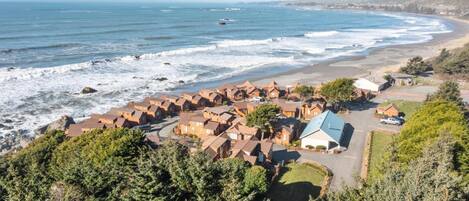 A coastal residential area with houses near the beach, a clear view of the ocean, and a hilly landscape in the background.