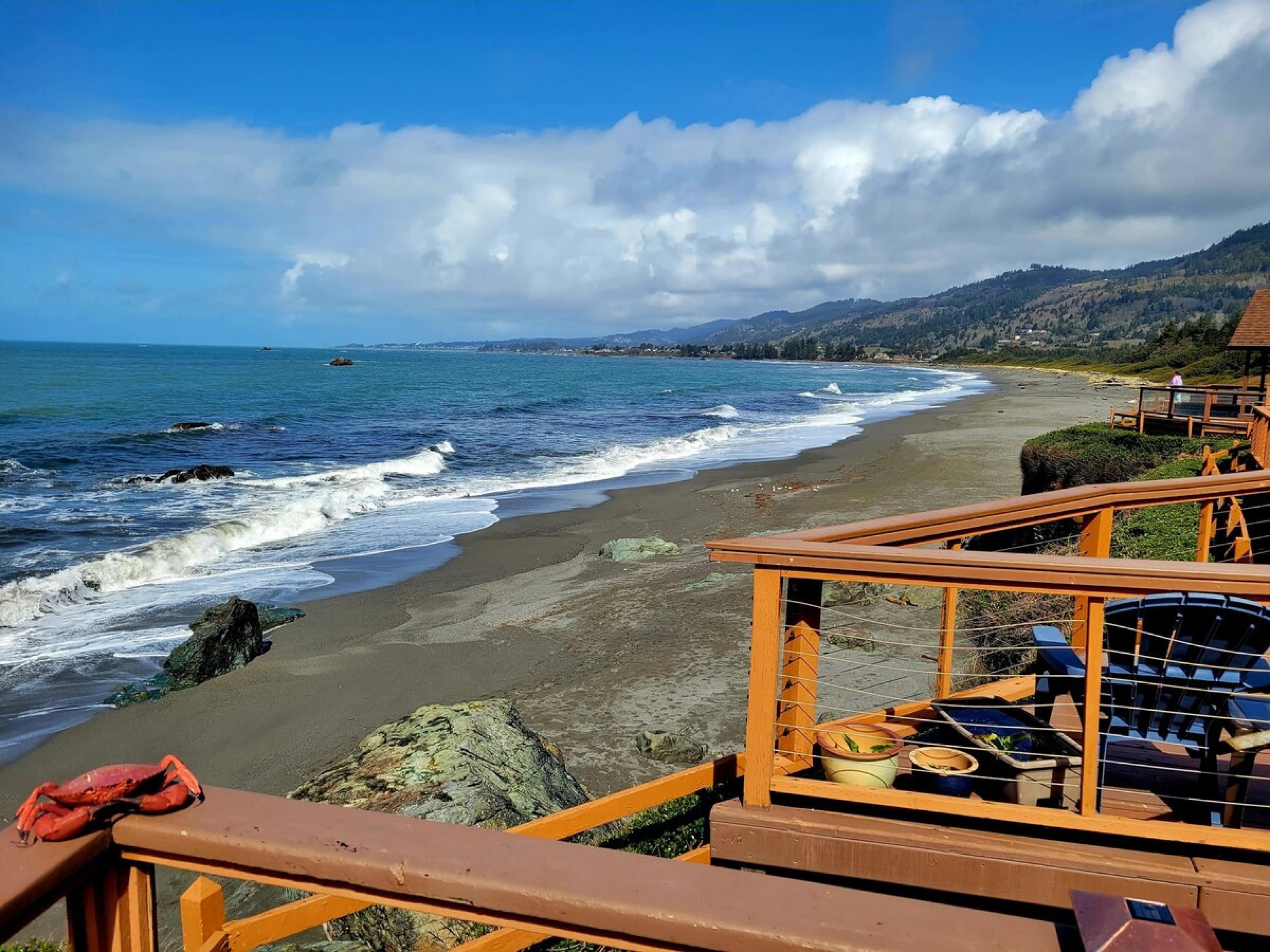 Vista a la playa con una terraza de madera y sillas de descanso.