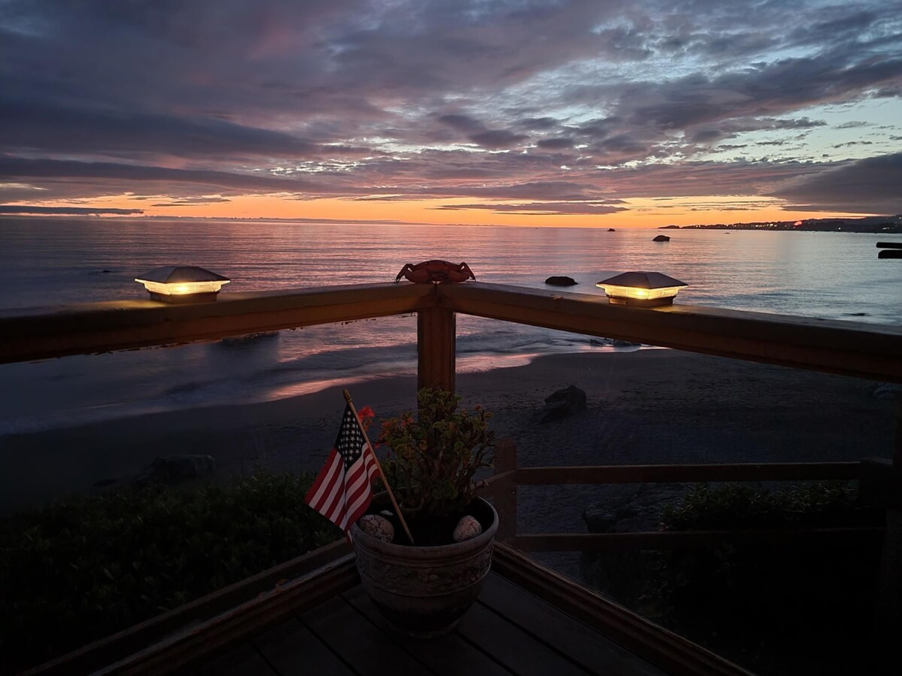 A sunset view from a balcony with a railing, a potted plant, and an American flag.