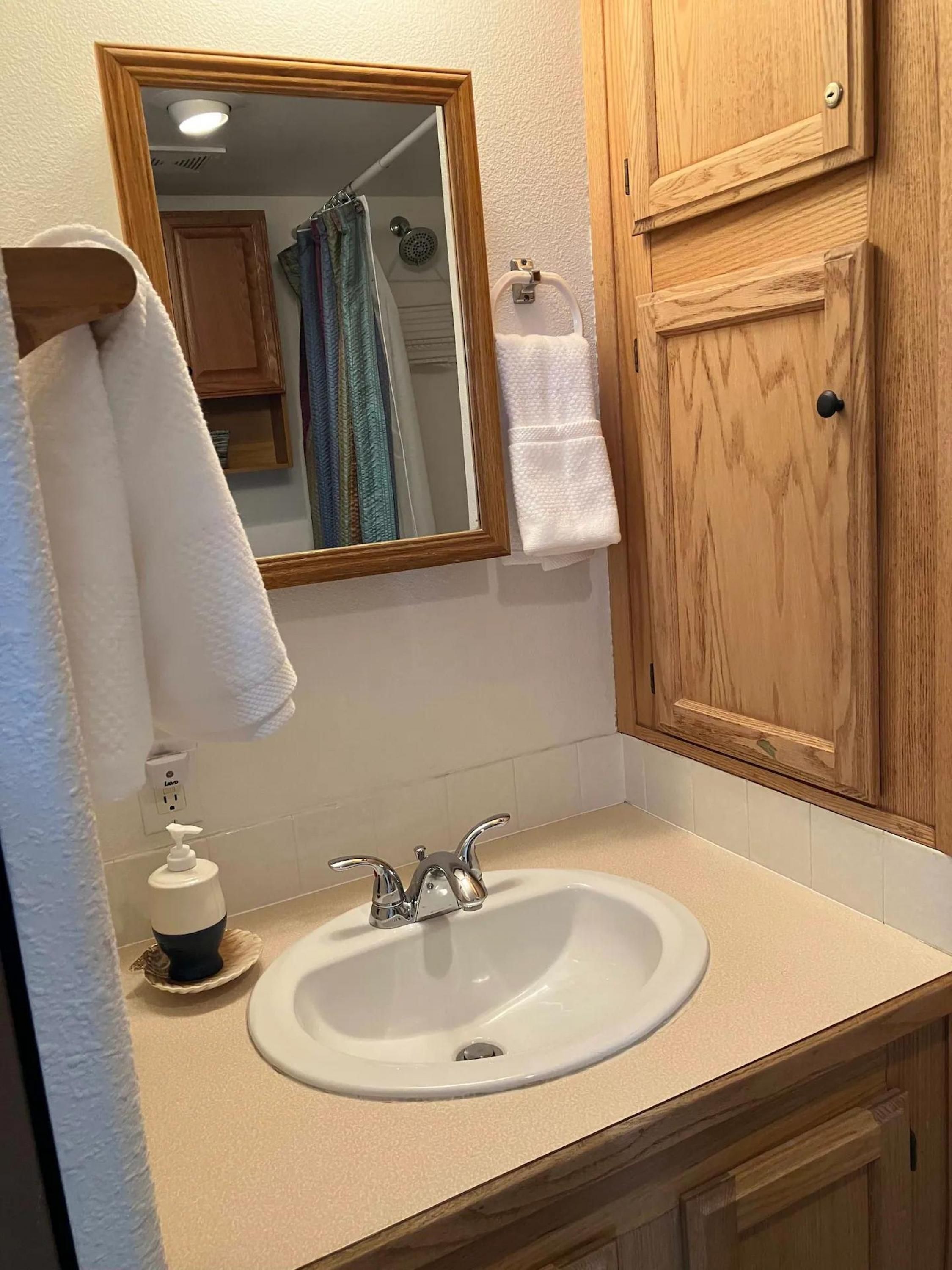 A bathroom with a white sink, a mirror, wooden cabinets, and a towel rack.