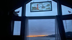 Una habitación con un ventanal grande con vista a una playa al atardecer.