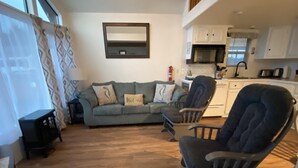 Una sala de estar con un sofá, un sillón mecedora y una cocina al fondo.