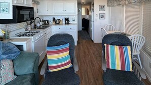 Cocina compacta con armarios blancos, estufa y comedor con dos sillas y un cojín colorido a rayas.
