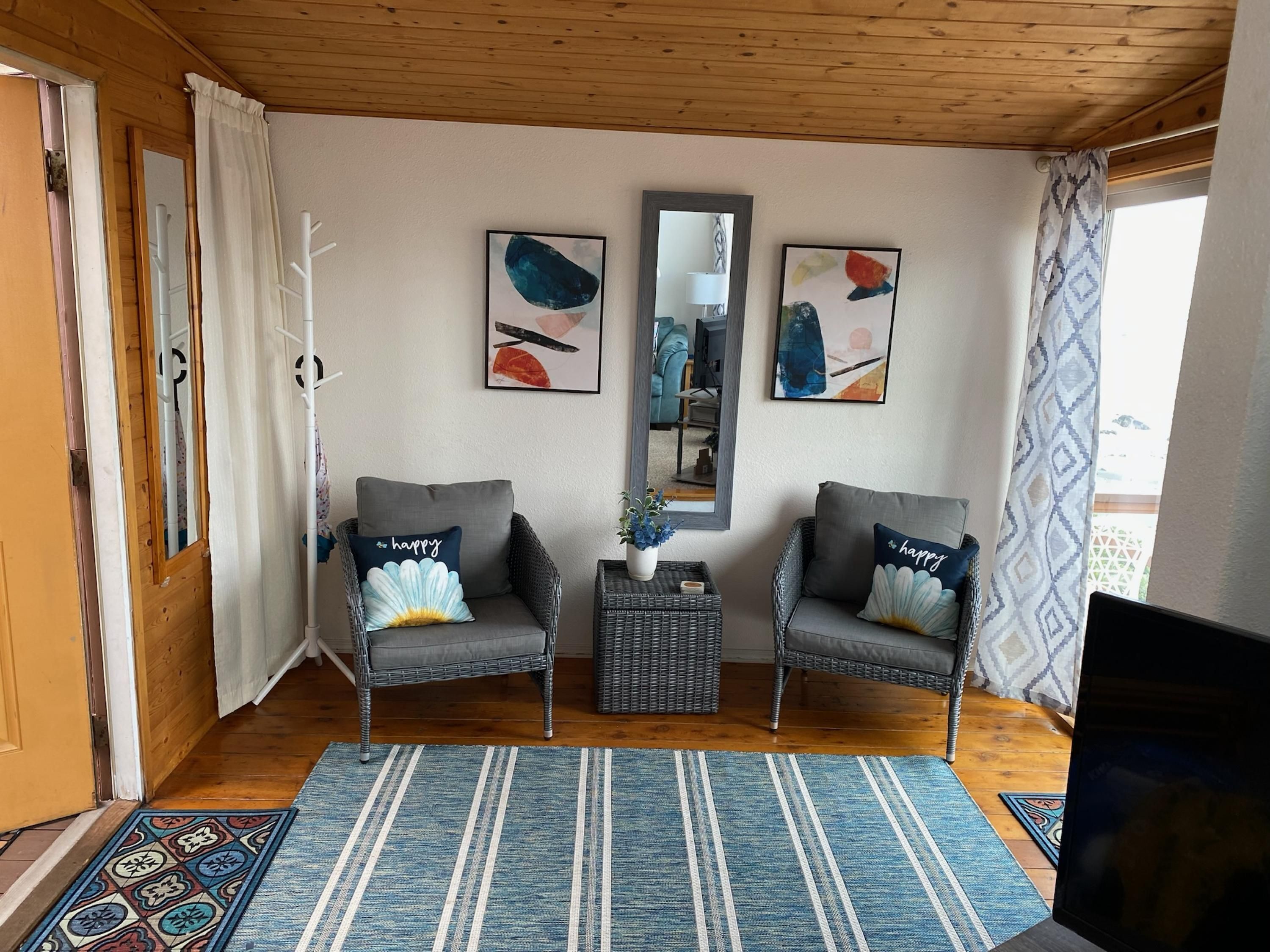 A cozy living room with two grey armchairs, a blue and white striped rug, and a large mirror on the wall.