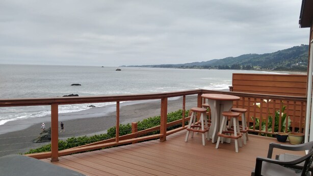 A wooden deck with a view of the ocean and hills. There are two white stools and a table. - Ocean Front Cabin 11 w Jacuzzi Superb Views (Smith River)