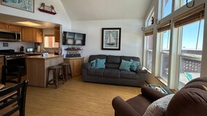 A spacious living area with a kitchen, a gray sofa with teal cushions, a wooden dining table with bar stools, and a ceiling fan. - Ocean Front Cabin 11 w Jacuzzi Superb Views (Smith River)