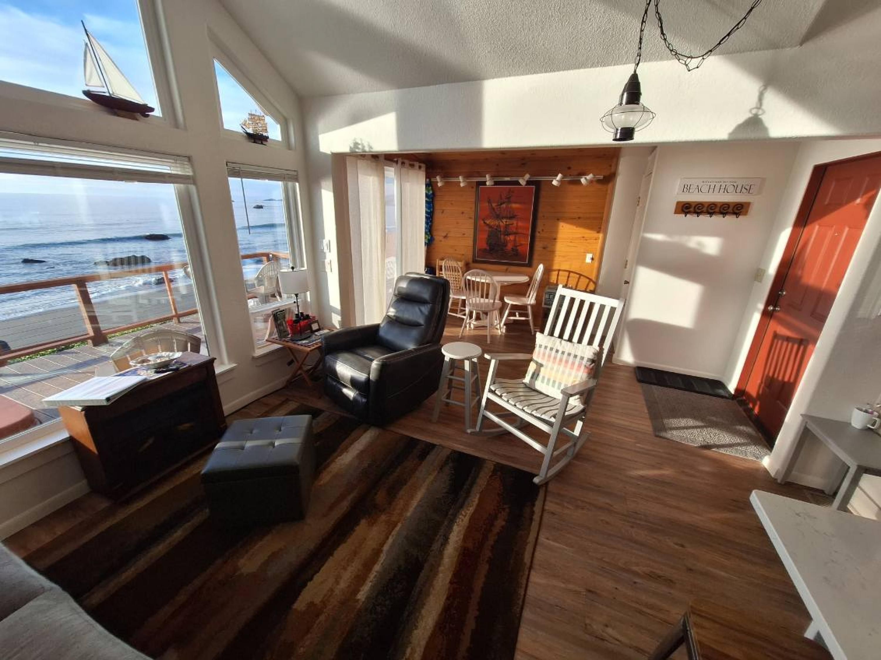 A cozy room with a view of the ocean, featuring a leather chair, a striped armchair, and a small table with a lamp.