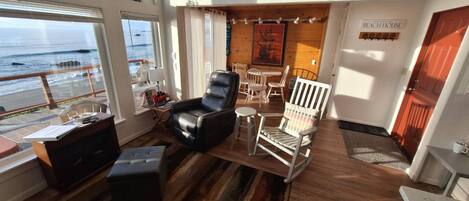 A cozy room with a view of the ocean, featuring a leather chair, a striped armchair, and a small table with a lamp.