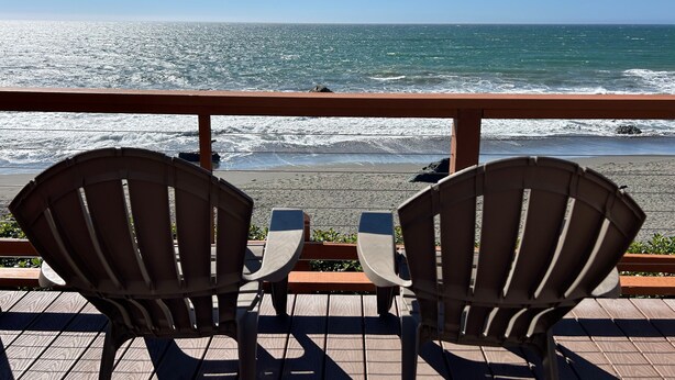 Due poltrone Adirondack rivolte verso una spiaggia con le onde che si infrangono sulla riva.
