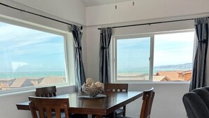 Ein Essbereich mit Holztisch und -stühlen, großen Fenstern mit Vorhängen und einem Deckenventilator.