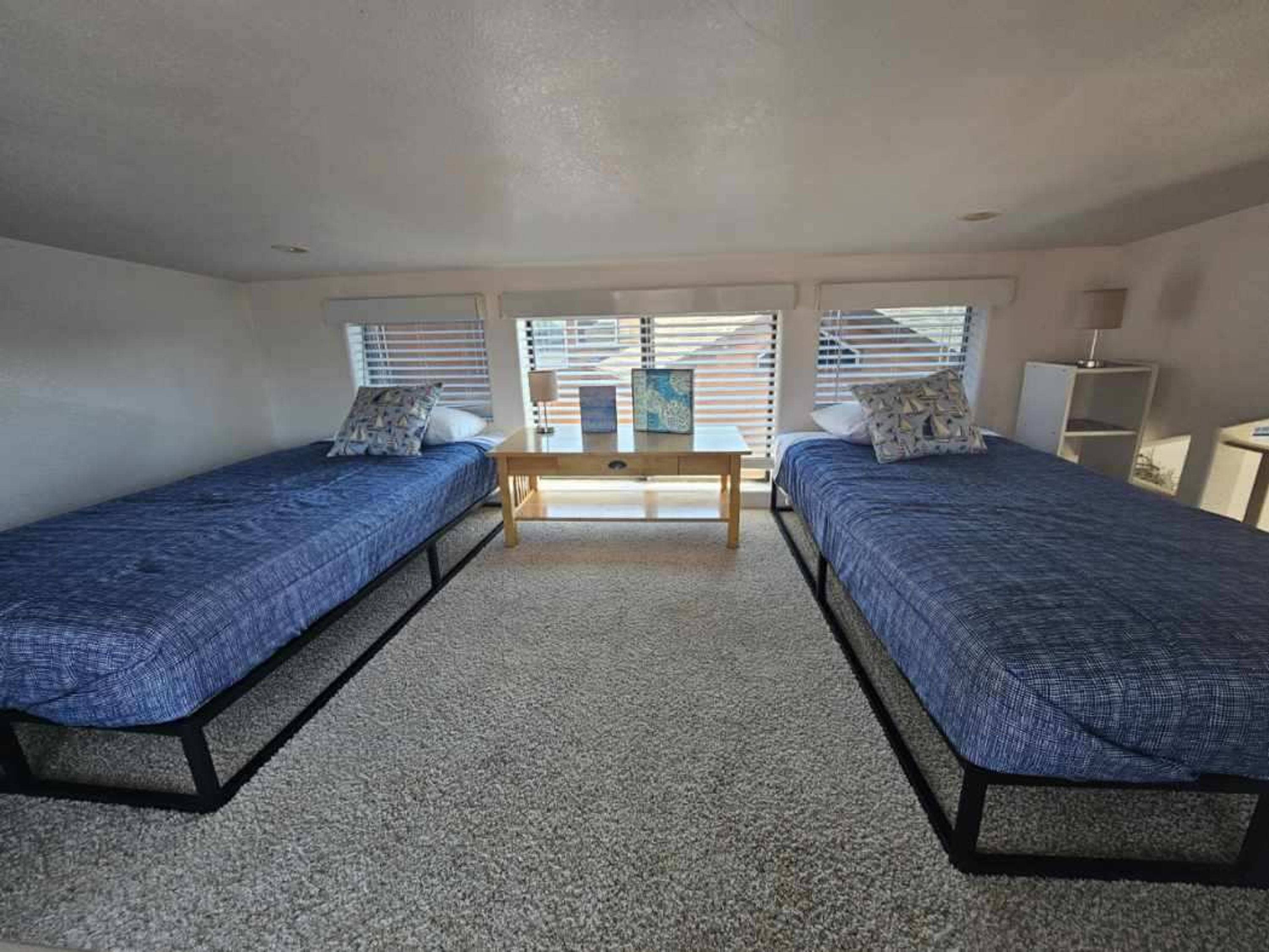 Habitación doble con dos camas individuales, una mesita y una ventana con persianas.