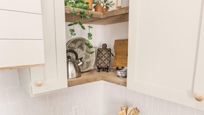 A kitchen with a wooden countertop, white cabinets, and a shelf with plants and kitchenware. - Evangeline A in Lafayette (Lafayette)