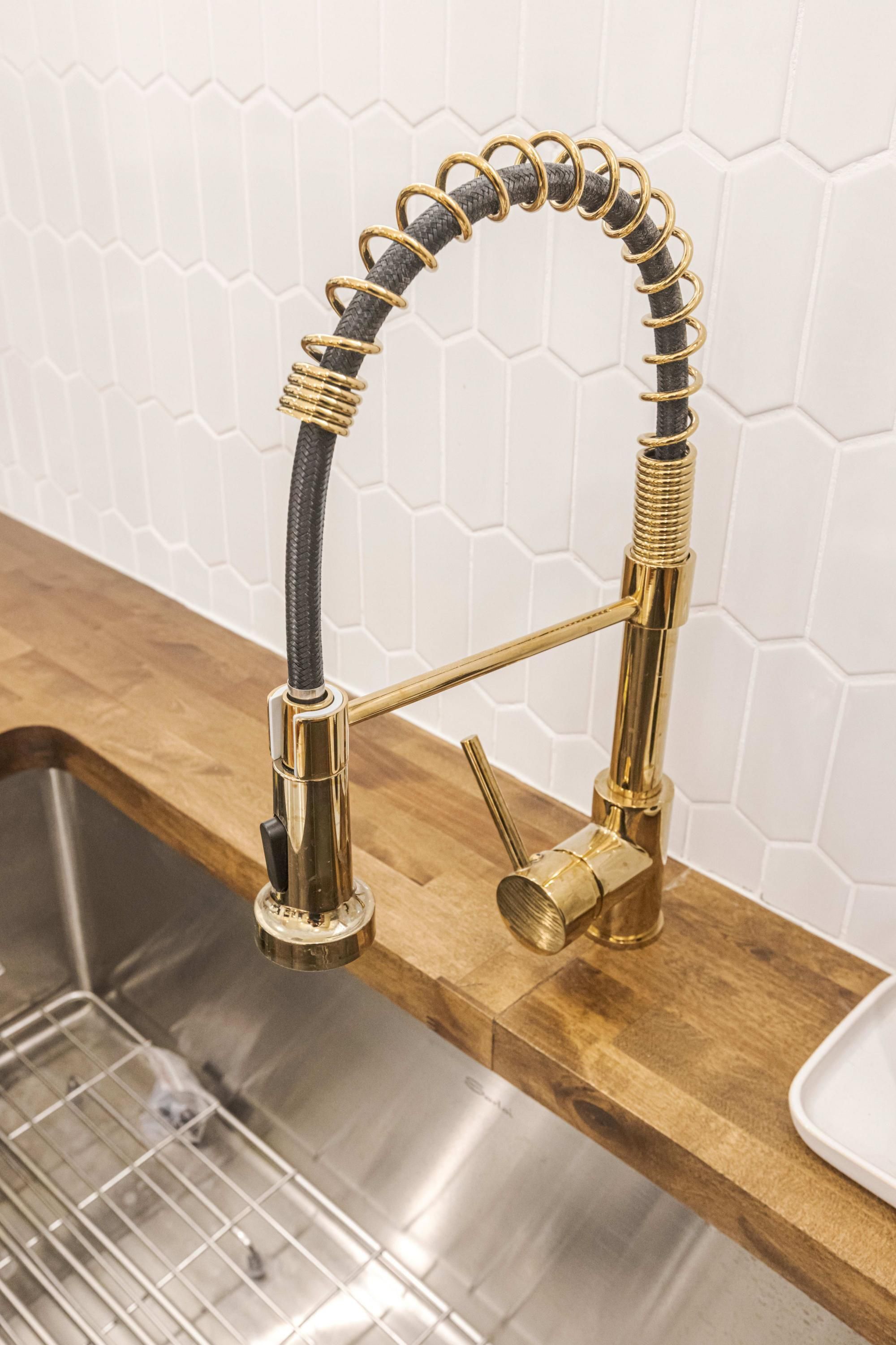 A kitchen with a stainless steel sink, a gold-colored faucet, and a wooden countertop.