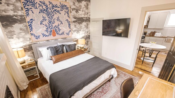 A modern bedroom with a bed, bedside tables, a TV, and a view into the kitchen. - Evangeline A in Lafayette (Lafayette)