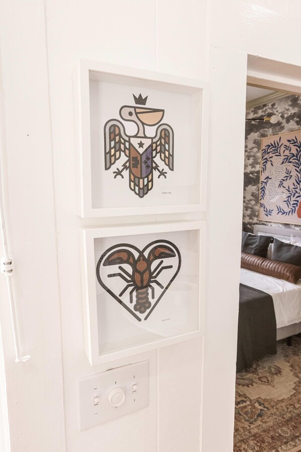 Two framed artworks on a wall, a bird with a crown and a heart with a lobster, in a room with a bed and a patterned rug. - Evangeline A in Lafayette (Lafayette)