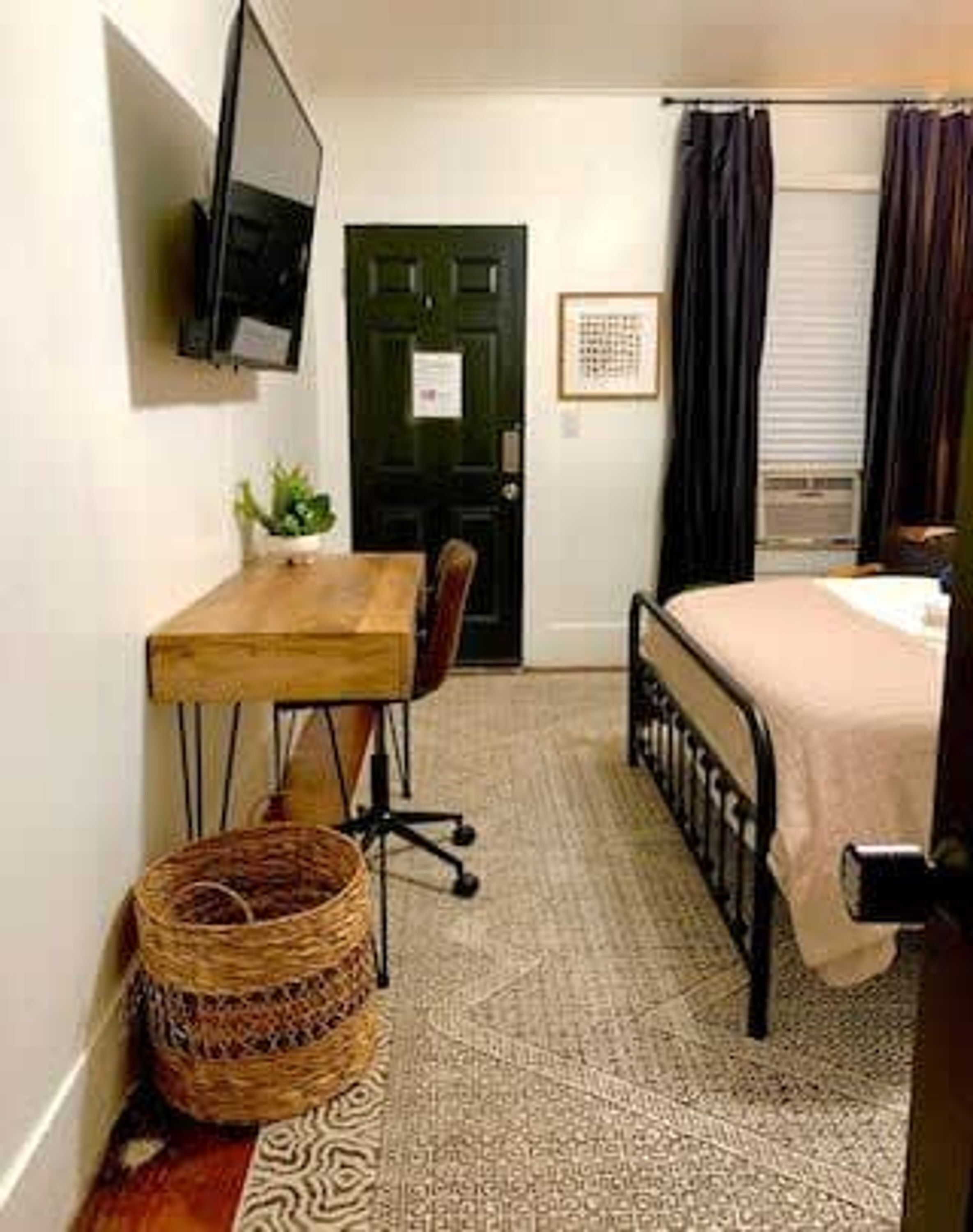 Une petite pièce bien rangée, avec un lit, un bureau, une chaise, un téléviseur et une porte.