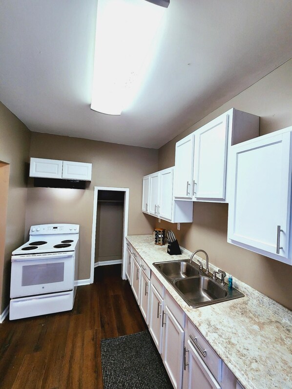 A compact kitchen with white cabinets, a stainless steel sink, and a white stove. - Magnolia House in Lafayette (Lafayette)