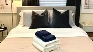 Una cama bien tendida con almohadas y una toalla doblada sobre un edredón de color claro.