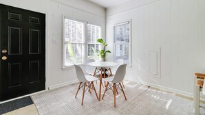 Una habitación con una puerta negra, paredes blancas, una mesa redonda con sillas y una planta en maceta.