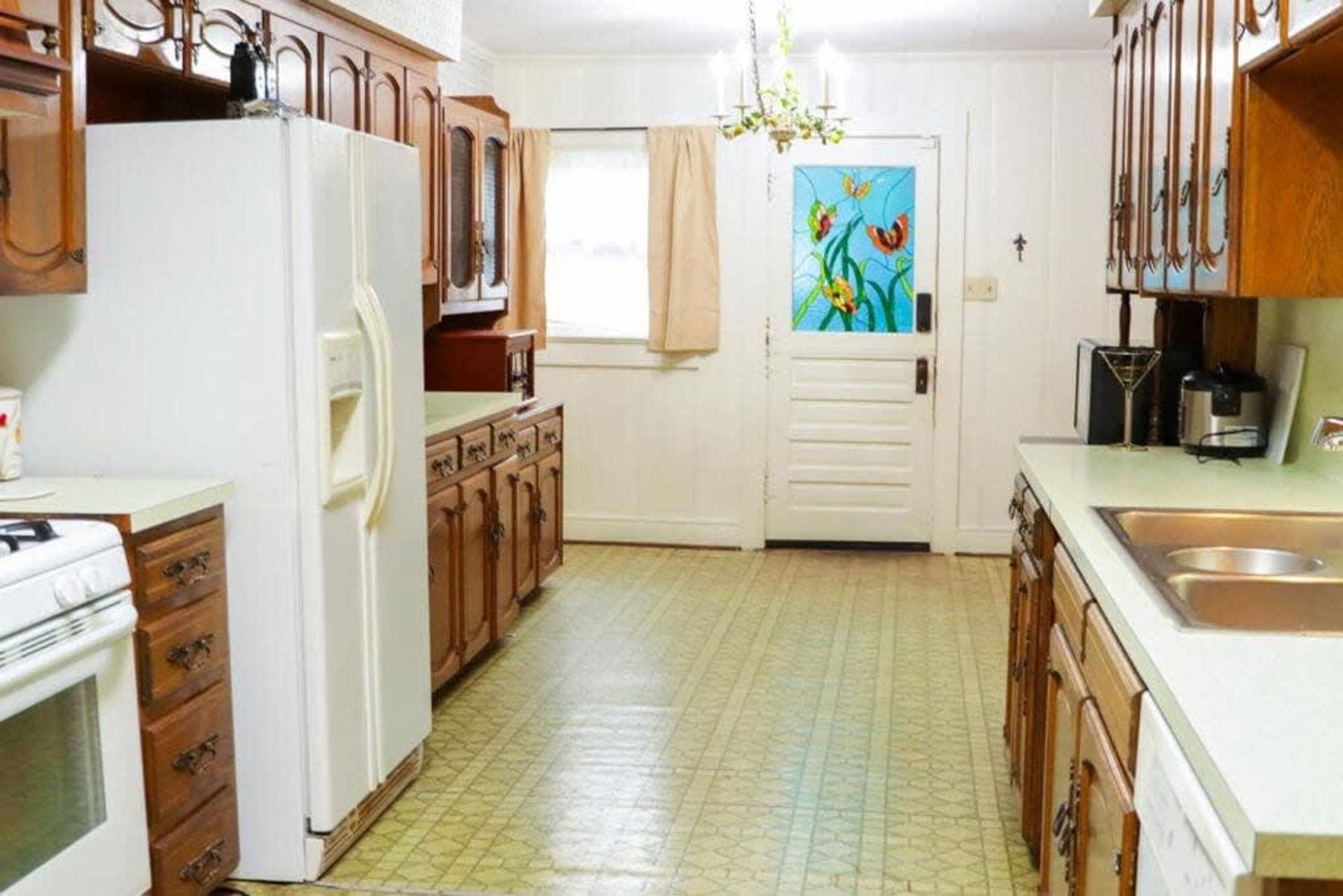 Una cocina con armarios de madera, un refrigerador blanco, una estufa y una ventana con cortina.