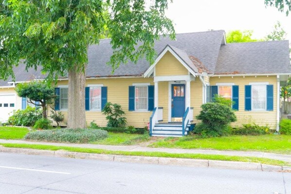 A yellow single-story house with a front porch, blue shutters, and a small front yard.
