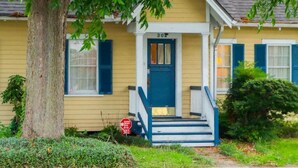 Una casa amarilla con puerta azul y escalones, número 302, rodeada de vegetación.
