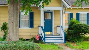 A yellow house with a blue door and steps, number 302, surrounded by greenery. - Corporate Comfort Ideal Accommodation for Work Crews (Lafayette)