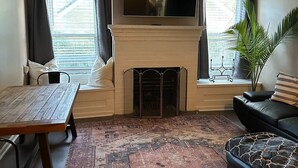 A living room with a fireplace, a ceiling fan, a flat-screen TV, a dining table, and a sofa. - Corporate Comfort Ideal Accommodation for Work Crews (Lafayette)