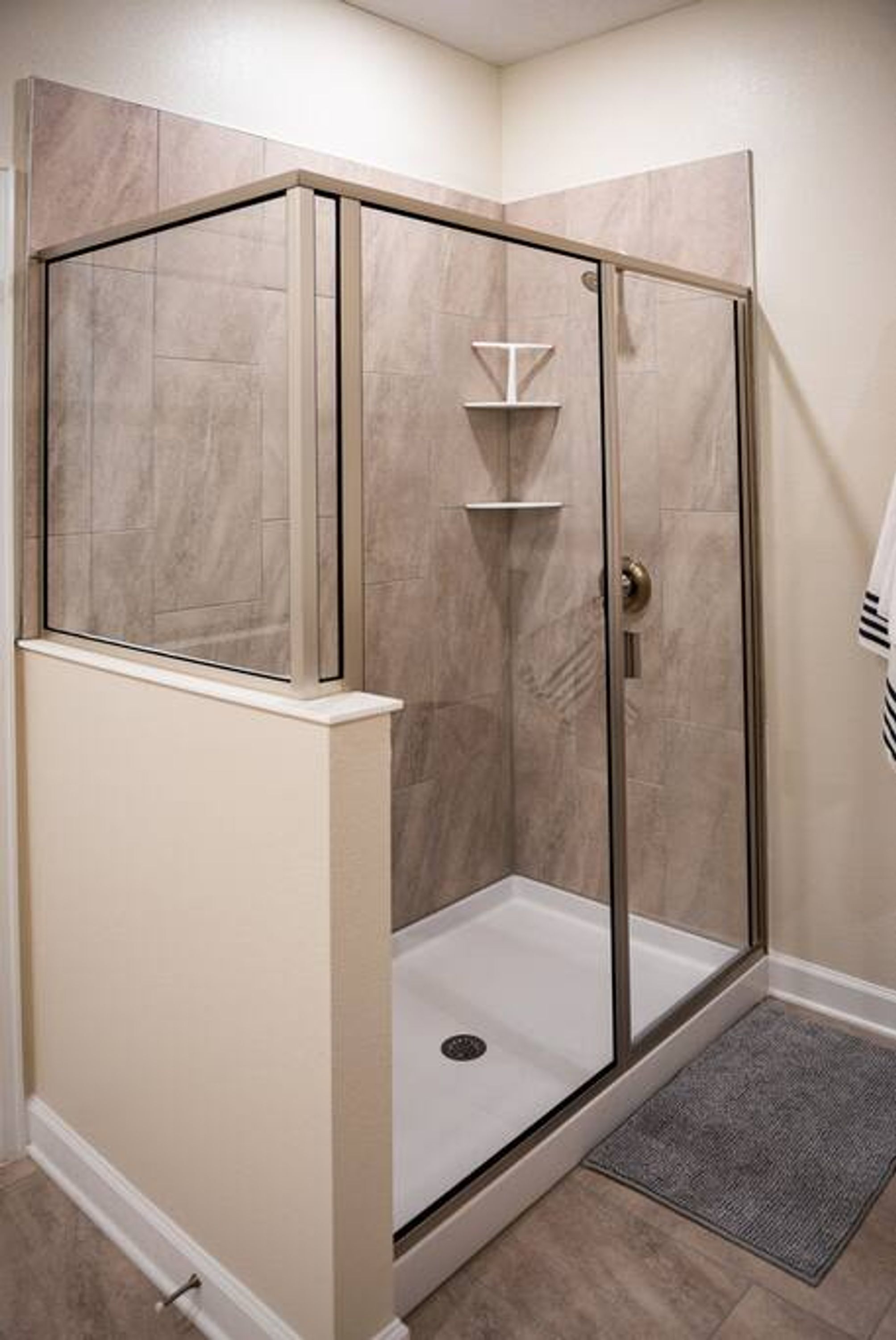A corner shower with glass doors and a white base, tiled walls, and a small shelf.