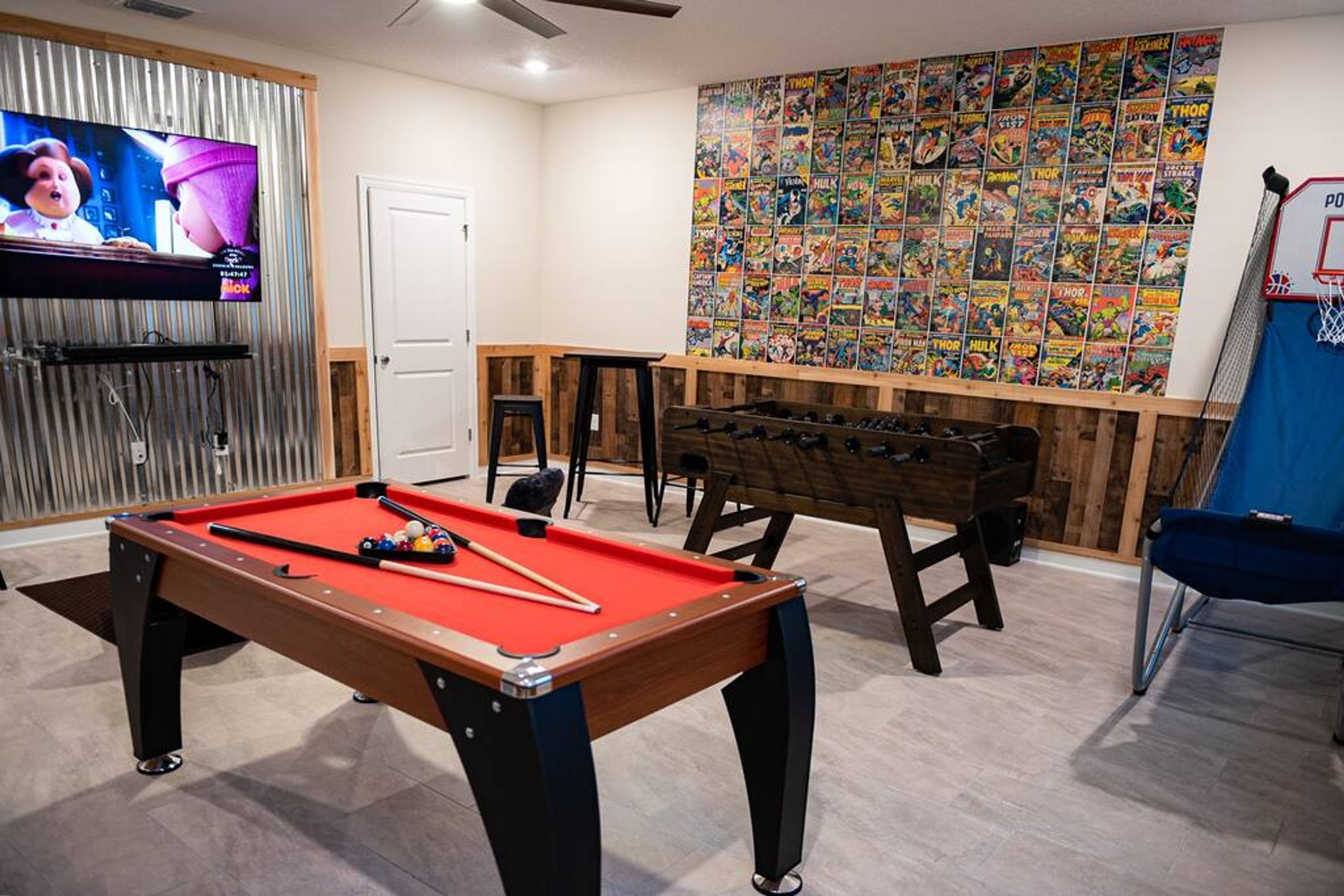 Una mesa de billar, una mesa de fútbol de mesa y una pared decorada con carteles de historietas.