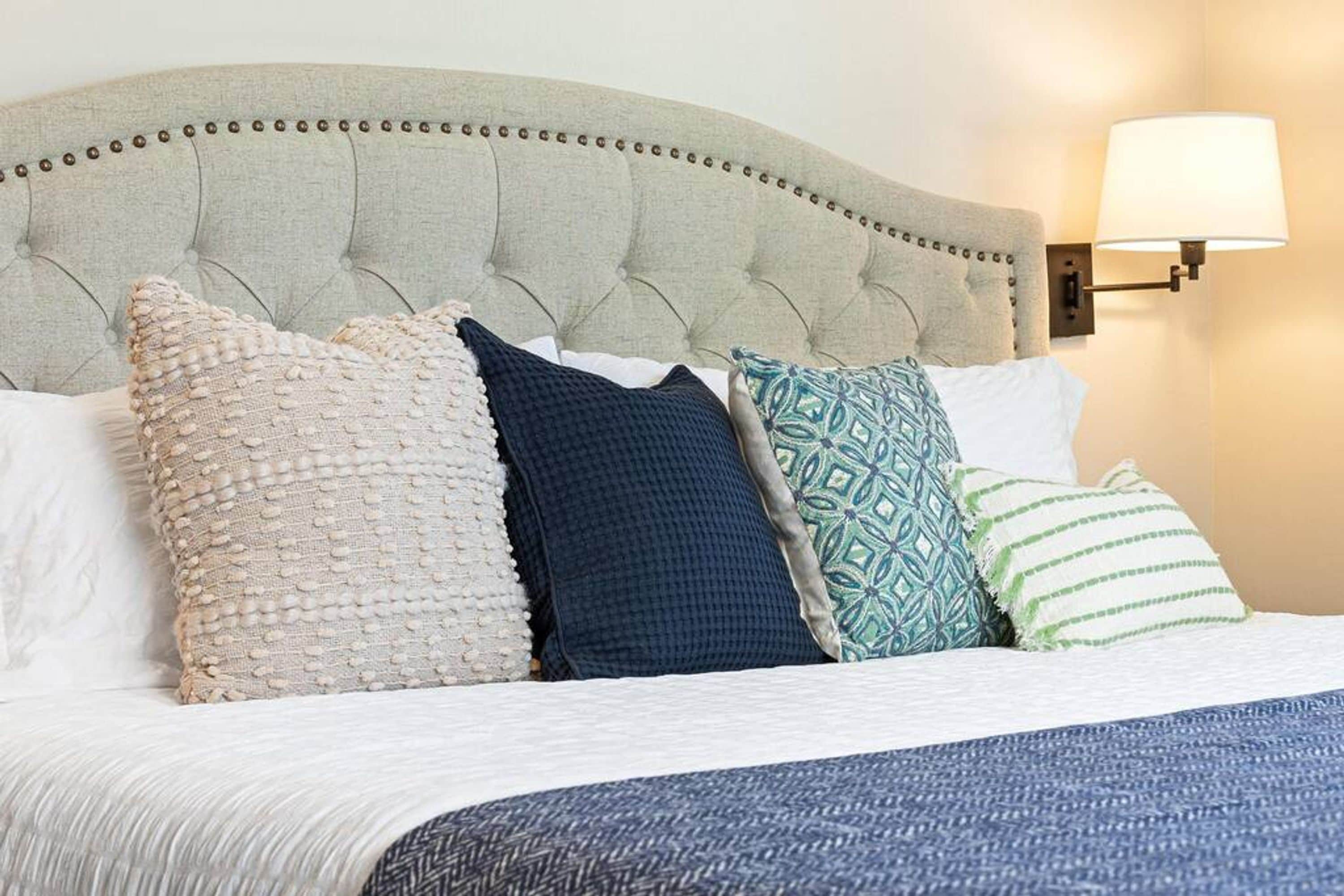 A bed with a tufted headboard, multiple pillows, and a wall-mounted lamp.