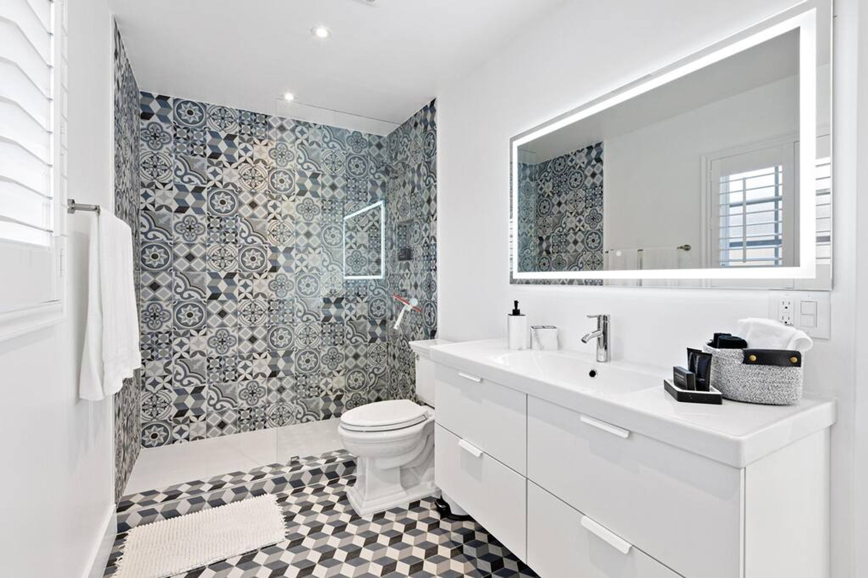 A modern bathroom with patterned tiles, a white sink, and a large mirror.