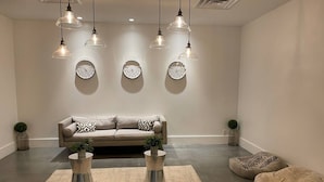 Un salon moderne avec un canapé beige, deux tables basses en métal, un tapis rond et trois horloges murales.