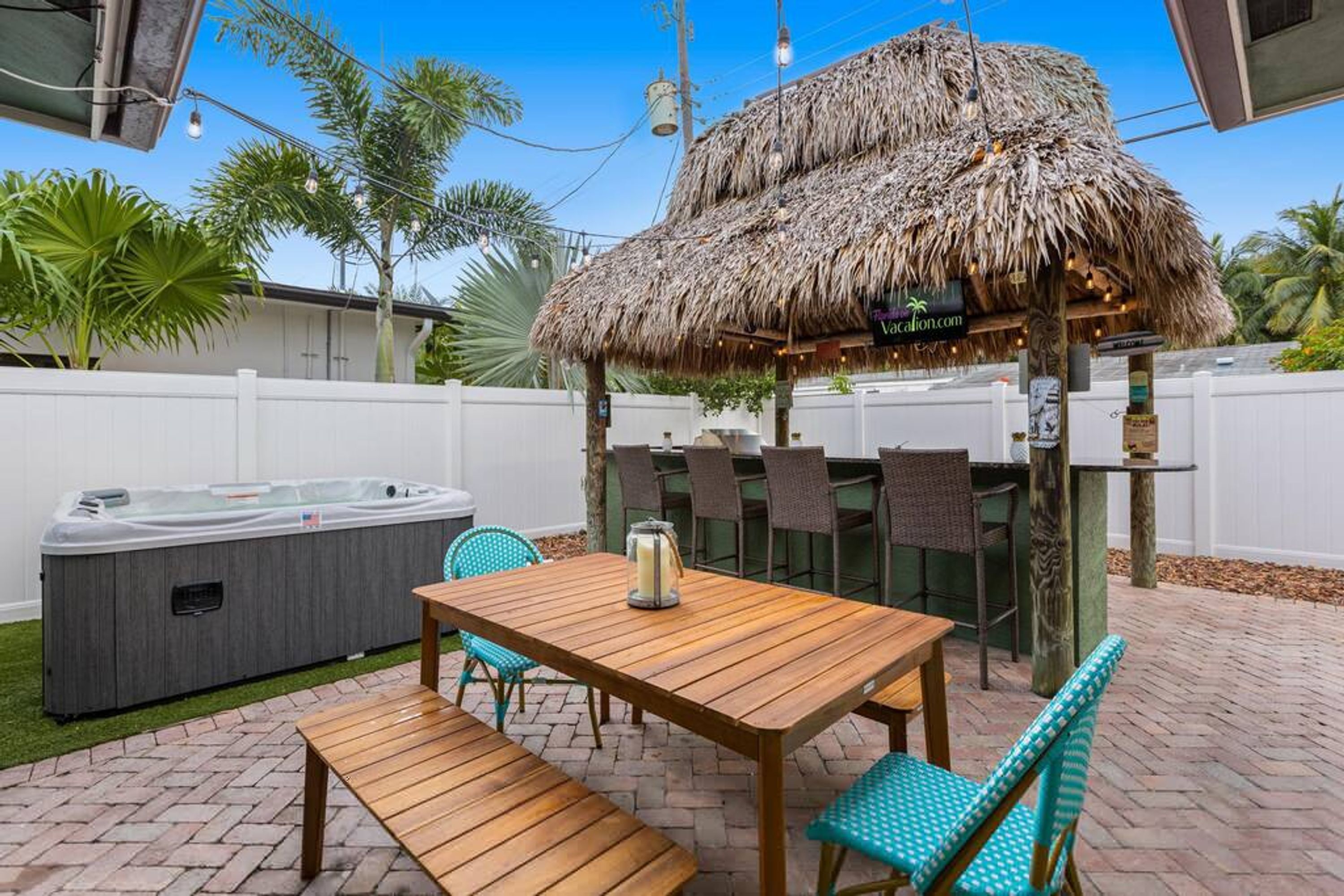 Un espace patio avec une table et des chaises en bois, un jacuzzi et une structure dotée d’un toit de chaume.