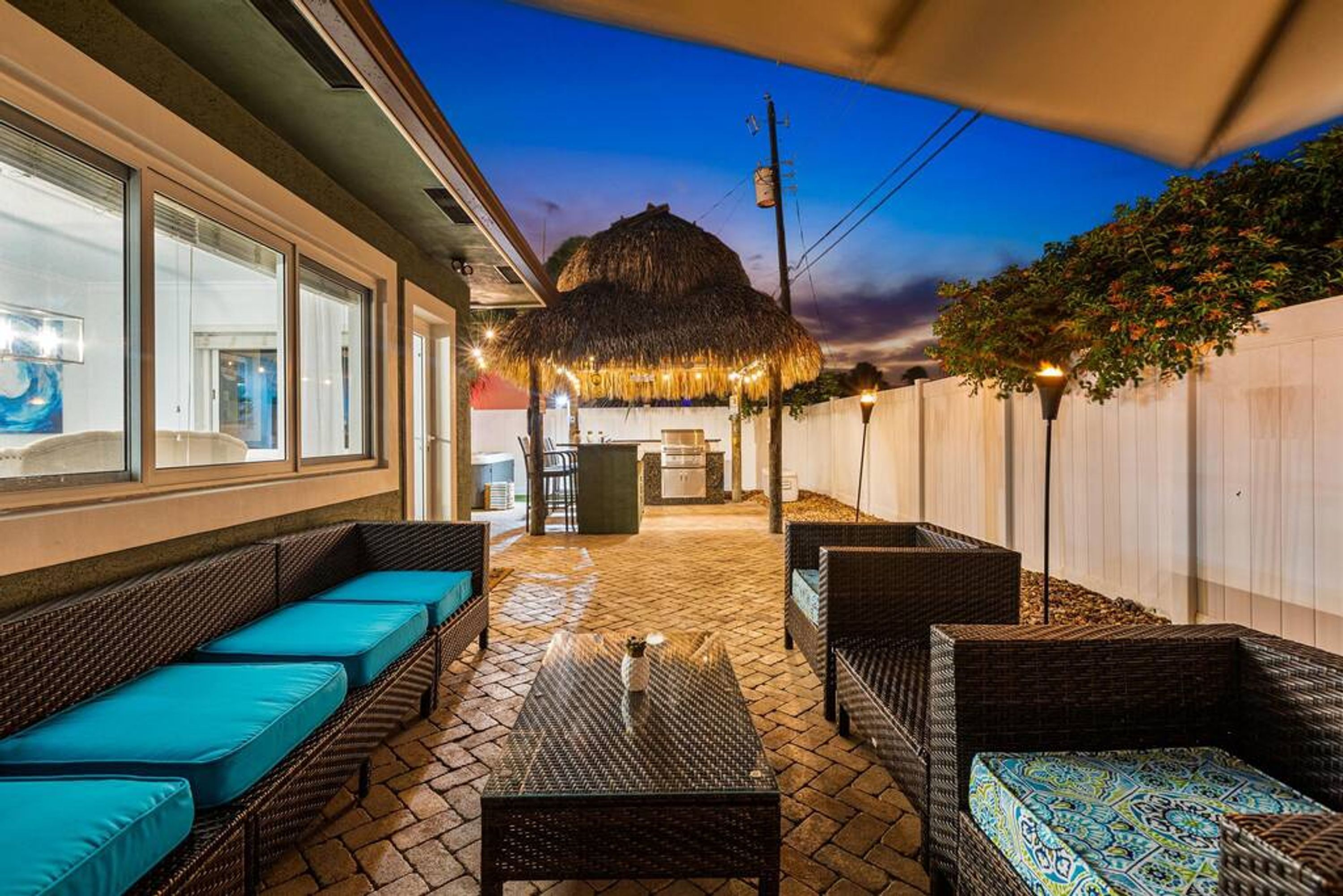 An outdoor patio with wicker furniture, a thatched-roof structure, and a view of the evening sky.