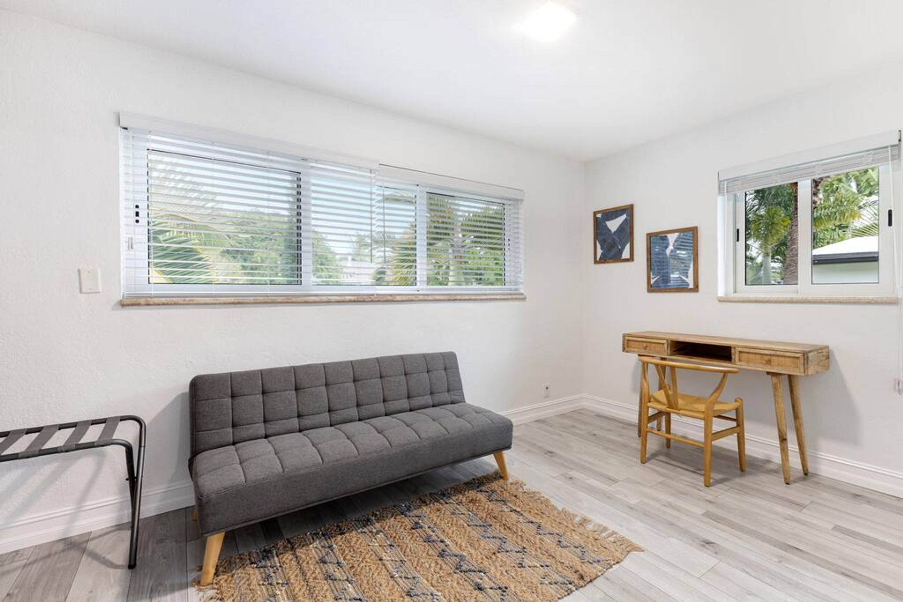A room with a grey sofa, a wooden desk, and a window with blinds.