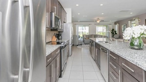 A modern kitchen with stainless steel appliances, dark wooden cabinets, and a granite countertop. - Luxurious Villa 9br Encore Resort Near to Disney (Kissimmee)