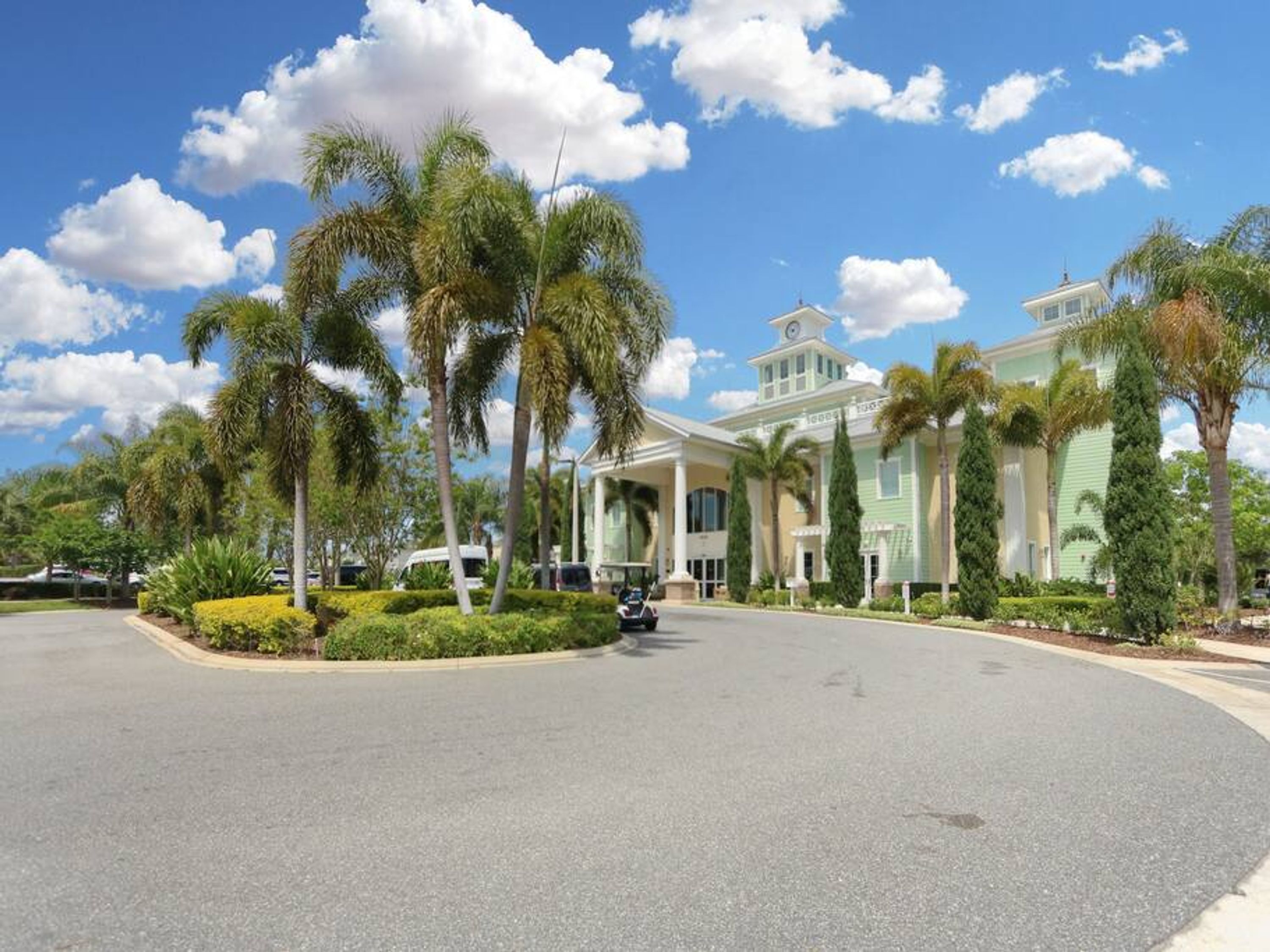 Un hotel con un'ampia strada d'accesso, palme e un cielo azzurro limpido.