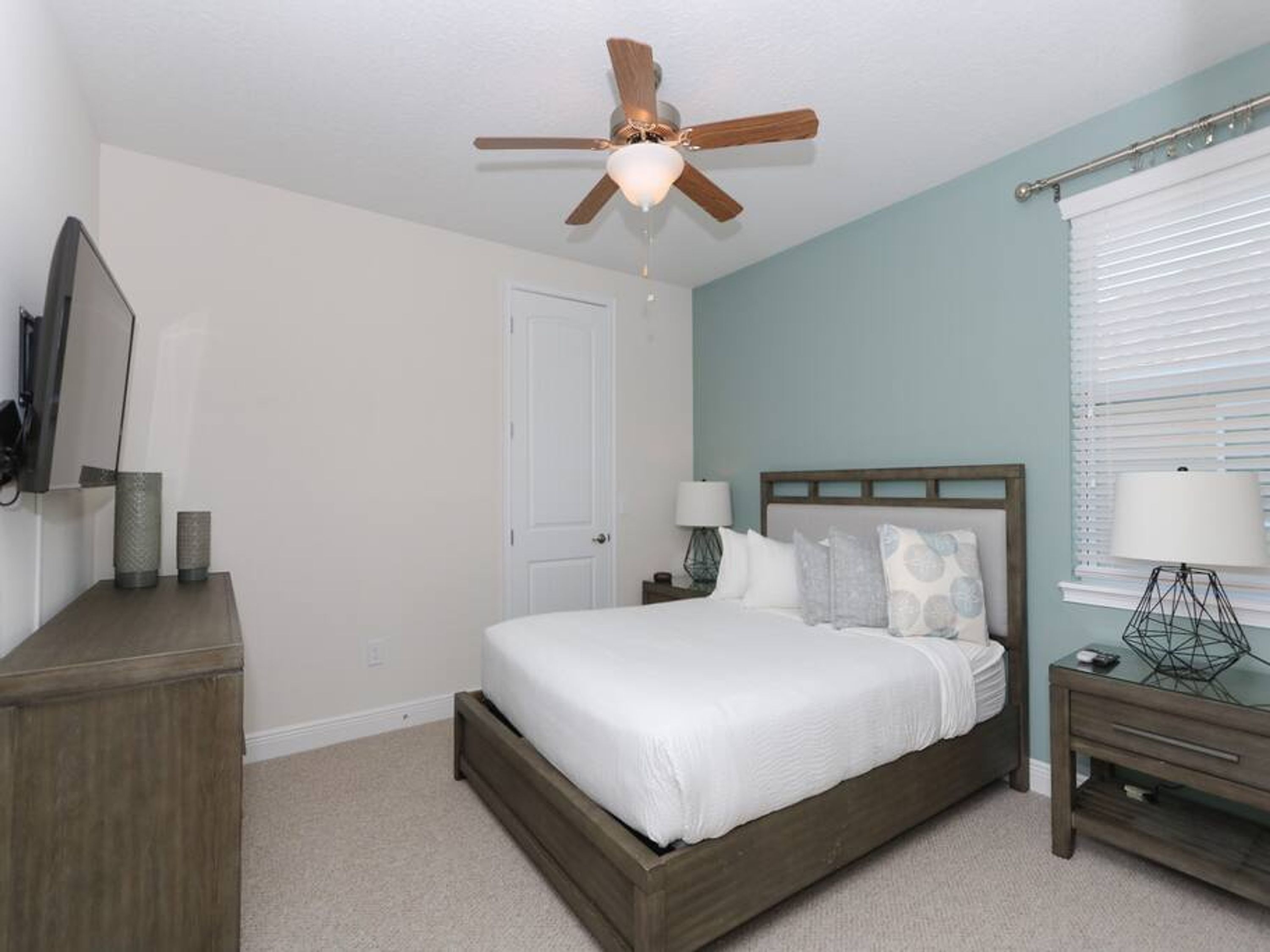 Une chambre à coucher comprenant un lit, un ventilateur de plafond, une table de chevet, une lampe et une commode.