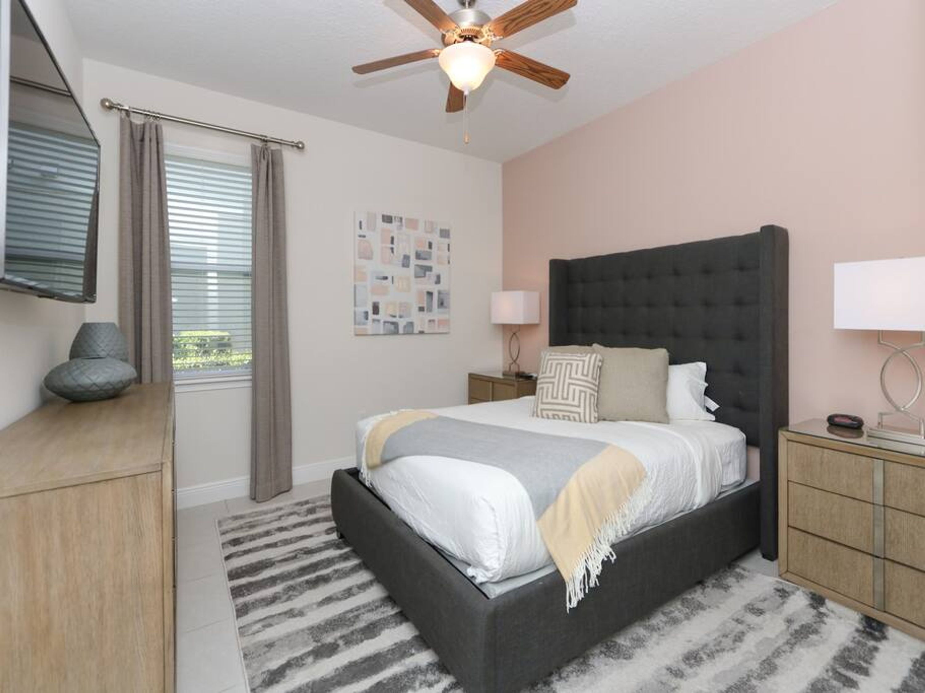 A bedroom with a bed, a ceiling fan, a window with blinds, a bedside table, and a nightstand.